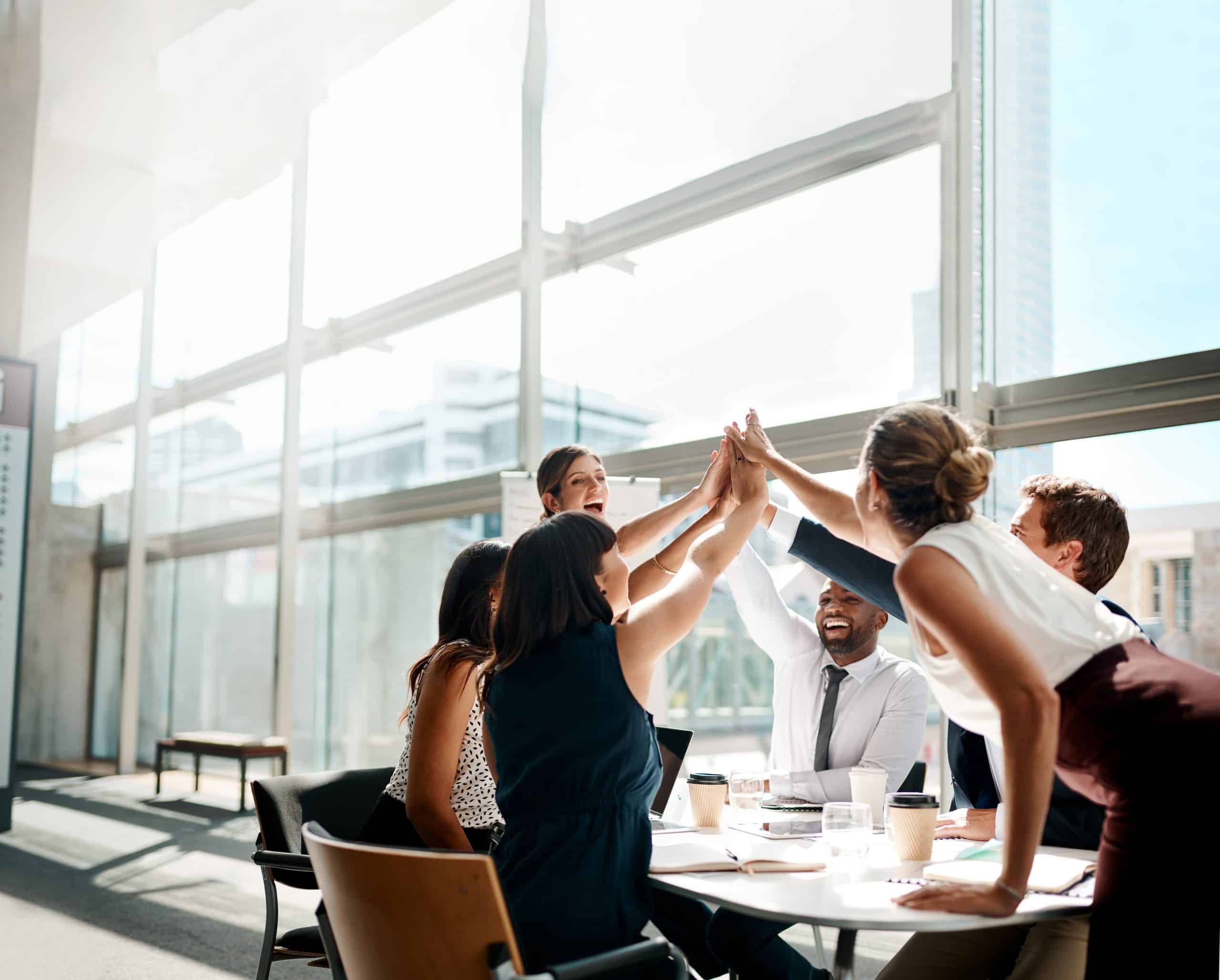 Shot of a group of businesspeople high fiving while sitting in a meeting