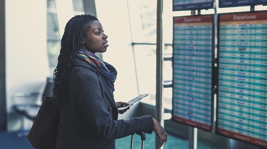 Young African American woman at airport checks the arrivals and departures board