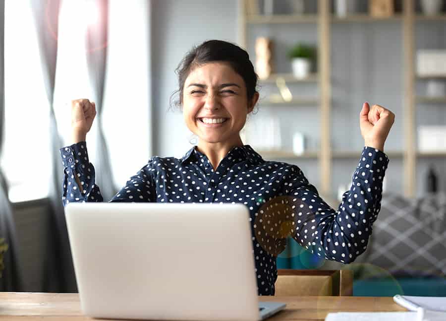Euphoric young indian girl student winner celebrate victory triumph sit at home desk with laptop computer win online fortune feel excited get new job opportunity good exam result great news concept