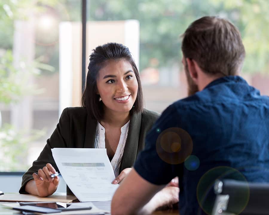 Hispanic businesswoman smiles while showing a document to a male associate.