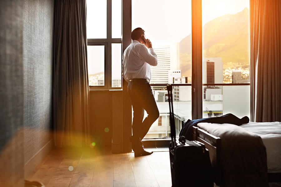 Rearview shot of a businessman looking through a hotel room window and talking on a cellphone
