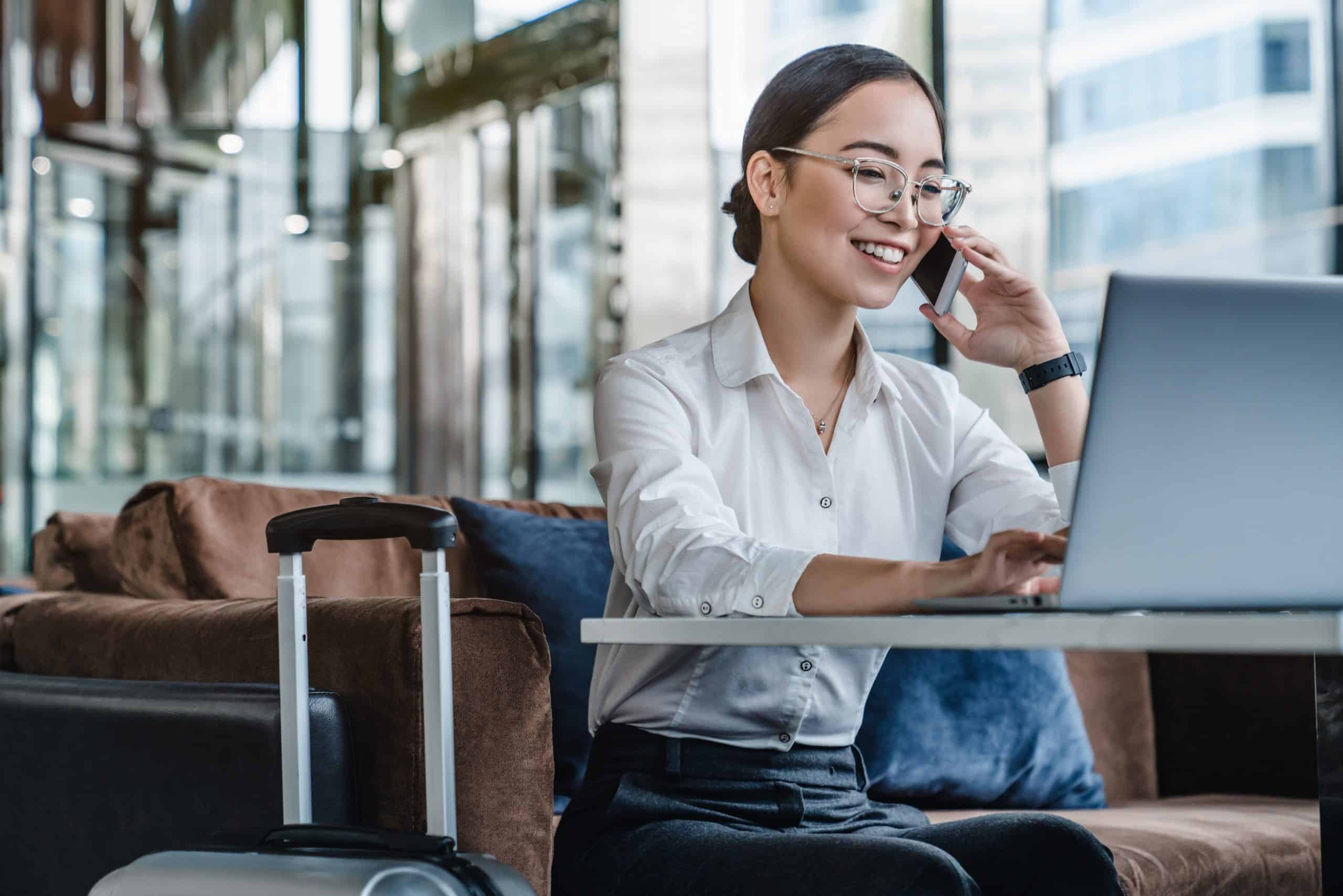 Asian female sitting at airport before trip having telephonic conversation with client and smiling. corporate travel management