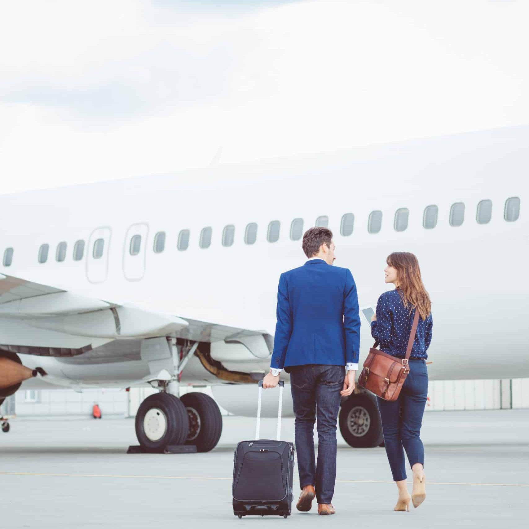 Rear view of two business colleagues walking together on tarmac at the airport. Business trip, people walking towards the airplane with luggage.